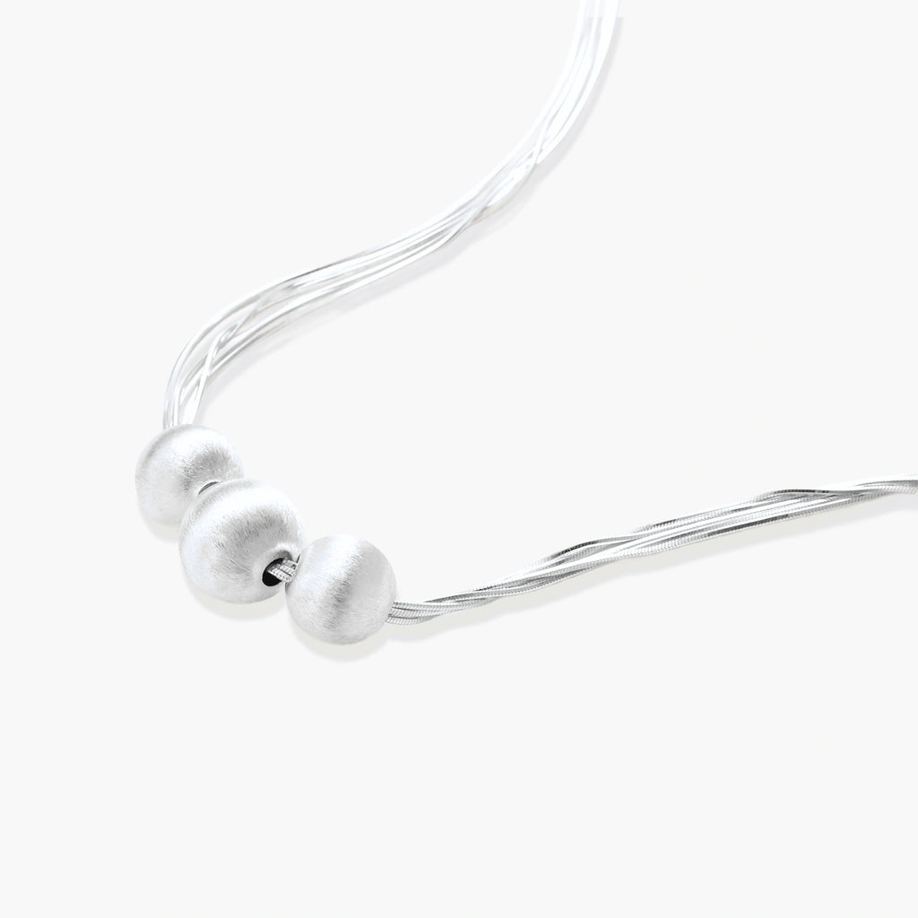 Sterling silver multi-strand necklace with three brushed round beads on cream background